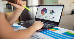 Person analyzing charts and graphs on a laptop while reviewing data reports.