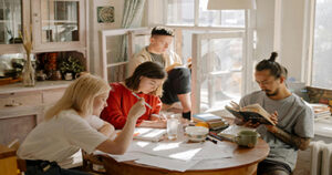 Group of students studying together around a table with books and notes in a bright room.