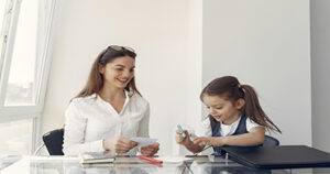 Teacher helping a young student with a learning activity at a desk.