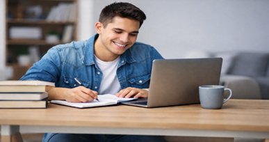 Student studying at a desk while writing notes and using a laptop with books and a coffee mug nearby