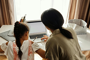 Mother and daughter using a laptop together at a home desk