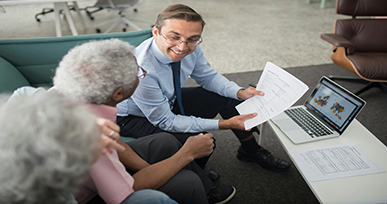 Professional showing documents and charts on a laptop while discussing information with two clients