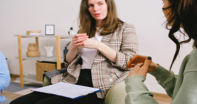 Two people engaged in a counseling or discussion session while one person holds a clipboard with notes.