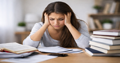 Stressed student sitting at a desk with books and papers while studying.