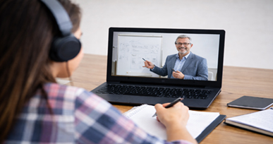 Student wearing headphones attending an online class on a laptop while taking notes