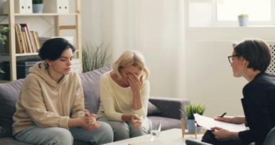 Two people sitting on a couch during a counseling or therapy session with a professional taking notes.