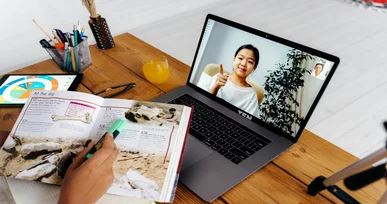 The image shows a person studying with a highlighter in a textbook while attending an online class on their laptop.